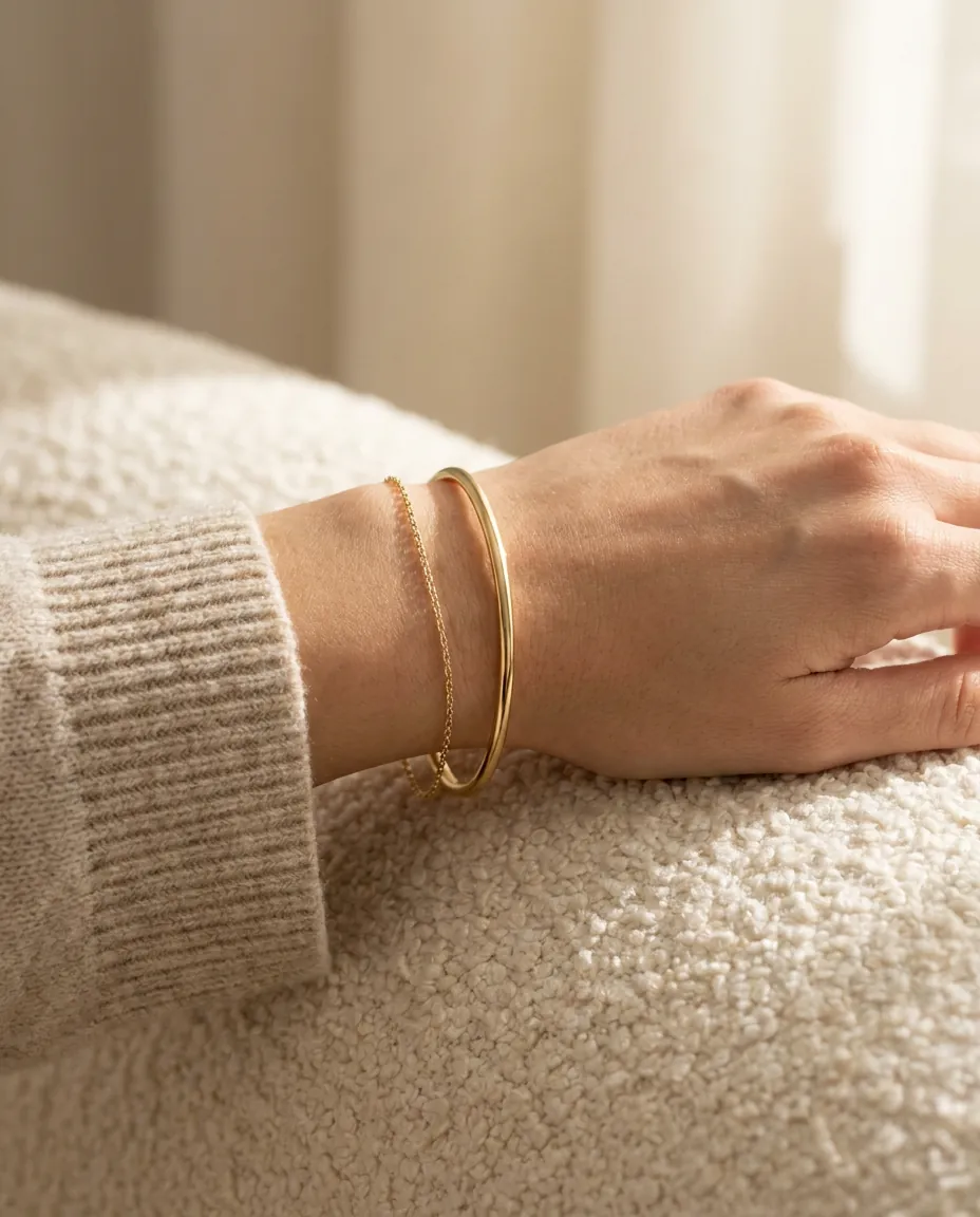 A gold bangle and a fine chain bracelet on a wrist