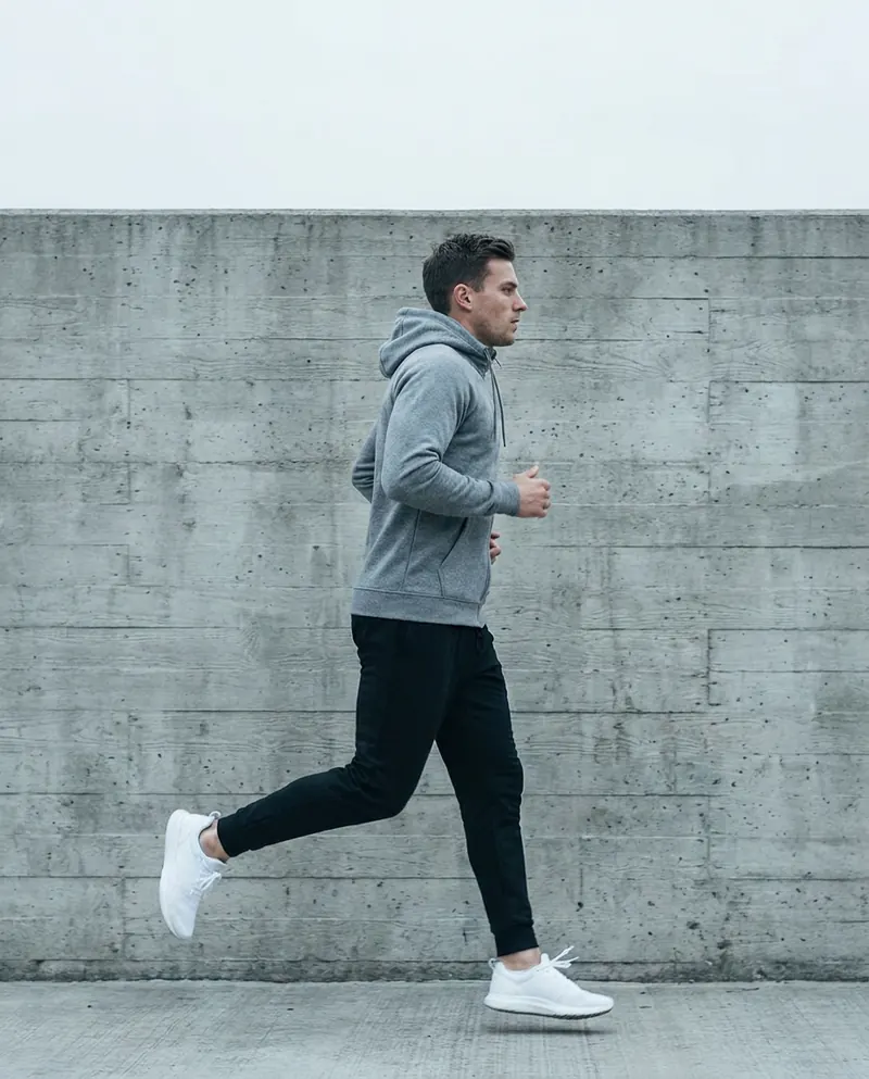 Runner in a grey hoodie and black joggers passing a concrete wall